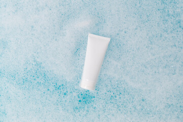A white tube in blue water with foam. Beautiful streaks on the water. The layout of the cosmetic product.