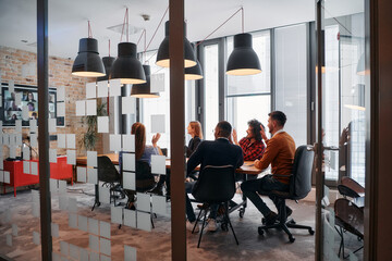 In a sleek glass office space, a team of business professionals engage in lively discussions and exchange strategic ideas, showcasing collaboration and innovation at the heart of modern corporate