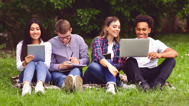 University students with devices preparing for classes, having break in campus, sitting on grass