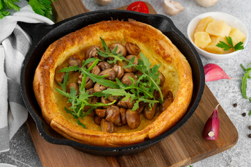 Savory Dutch baby pancake with cheese, fried mushrooms and arugula in cast iron pan on a concrete background. Vegetarian breakfast.