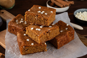 Pumpkin brown butter blondies or pumpkin cake with white chocolate drops and spices on a dark wooden background. Dessert for Thanksgiving or Halloween.
