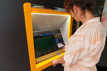 Hispanic Latin woman using ATM during daytime. Rear view.