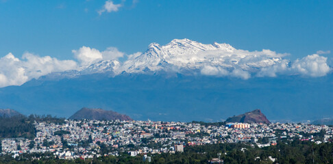 A mesmerizing view of Iztaccíhuatl, the majestic snow-capped volcano, towering over the bustling cityscape below.