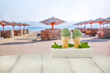Mint scoops of ice cream in waffle cones on a wooden table with a blurred tropical beach background. Summer concept and copy space for products.