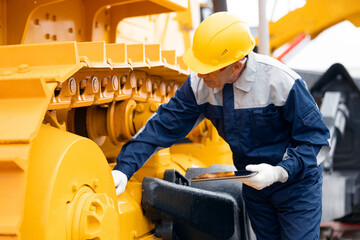 Repair of Industrial truck. Industry driver in hard hat with tablet computer checks breakdowns of excavator, bulldozer of mining © Parilov