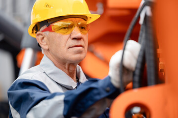 Mechanic repairing hydraulic hose in drilling machine, exploration drilling. Adult man in hard hat...
