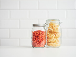 Dry pasta in reusable glass jars: wheat tagliatelle and red lentil fusilli. Kitchen pantry containers