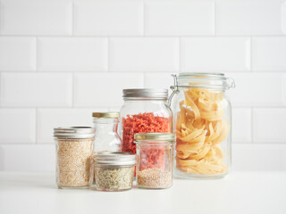 different glass jars with lids kitchen pantry containers with dry ingredients for cooking. Quinoa, flax, hemp seeds, dried pasta and spaghetti.