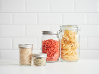 Red lentil pasta, dried spaghetti, quinoa and hemp seeds in different glass jars with lids. Reusable kitchen pantry containers.