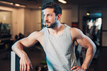 Male Athletic men with muscles, stand in gym and rest at a machine leaning against equipment, while...