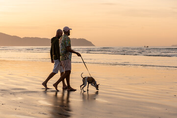 silhouette of a gay couple walking their dog on the beach at sunrise