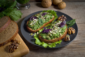 Toasts with homemade pesto sauce with sunflower seeds, sesame seeds and basil leaves on a dark plate