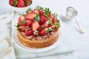 Strawberry cake. Homemade and delicious strawberry sponge cake with fresh summer fruits served, cream cheese frosting and sugar powder on white marble stand and wooden table. Summer berry dessert.