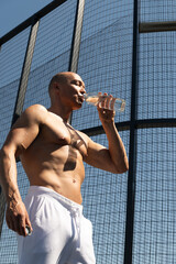 Athletes man holding glass bottle of water on outdoor sports ground. Concept water balance for hot season for active workout.