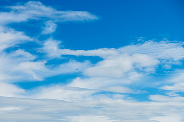 beautiful clouds in blue sky, natural background, small silhouette of a flying airplane against a background of blue sky with white clouds, wallpaper