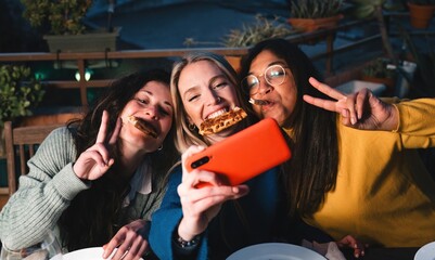 Young friends eating pizza in outdoor restaurant. Group of women having fun taking self photo together