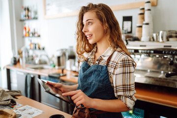 Young woman owner with tablet stands behind the counter of a coffee shop. Business concept. Takeaway food.