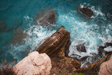 Helicopterview of cliff and rocks at the coast of the sea with rough waves and azure blue water