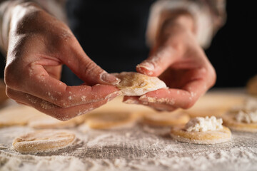 Woman making dumplings with cottage cheese on black background