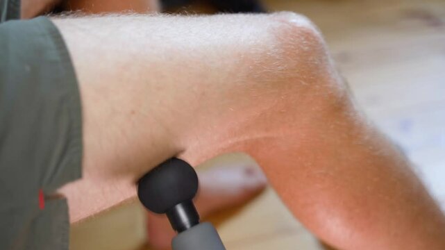 A man gives himself a percussion massage on the inside of his leg, close-up. Pain in the hamstring