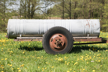 Obraz premium Water tank on wheels car trailer. Old metal rusty container. Meadow green grass. Animal feeding and watering. Fodd industry antique machine.