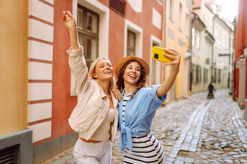 Portrait of funny pretty best friends women having fun making selfie at city center, positive crazy emotions, traveling together in Europe. Fashion, travel, blogging, technology concept.