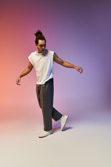 A young African American man dances in front of a colorful gradient background. He is wearing a white sleeveless shirt and gray pants.