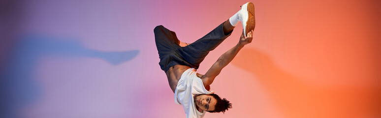 An African American young man dances against a vibrant gradient background, showcasing his...