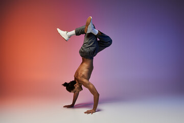 A young African American man performs a handstand while dancing against a gradient backdrop of red...