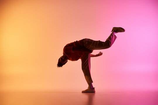 A young African American male dancer performs a dynamic pose against a colorful gradient background.