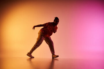 An African American male dancer performs a move against a gradient background of orange and pink.