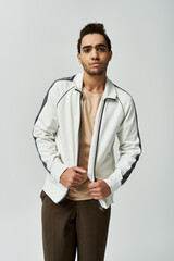 A young African American man poses in a stylish white jacket with black accents, against a grey background.