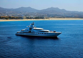 Luxury yacht sailing near the coastline with cityscape and mountains in the background.