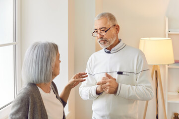 Fototapeta premium Portrait of senior elderly family couple wife and husband talking and discussing something in living room at home. Retired man and woman communicating indoors. Relationship in retirement concept.