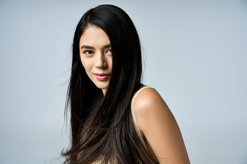 Fototapeta premium A young woman with long, black hair poses against a light grey background.
