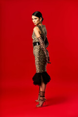 A young woman in a leopard print dress poses confidently against a red backdrop.