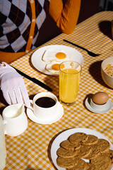 A woman dressed in a patterned sweater enjoys a breakfast of eggs, coffee, and cookies.