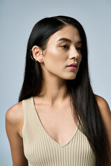 A young woman wearing a beige tank top poses in front of a plain background.