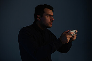 Serious young man playing video games isolated over grey background. Man stand all ears holding joystick console looking attentive try to win in the virtual world.
