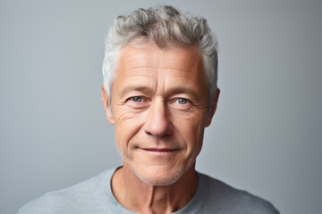 Confident mature man with grey hair. Portrait of mature man looking at camera and smiling while standing against grey background