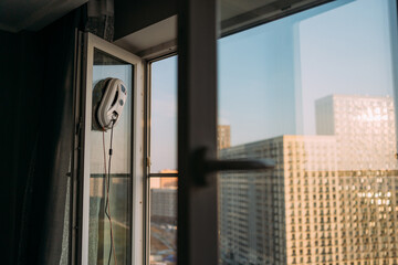 Robotic window cleaner operating on an open apartment window with cityscape background. Modern home technology, convenience, automated cleaning, and urban lifestyle
