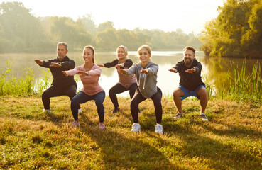 Group of positive athletes people performing squats exercise during outdoor workout, providing active and healthy lifestyle. Group fitness training in the city park showing teamwork.