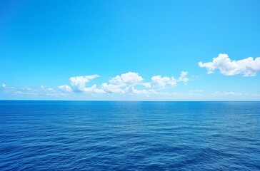 Obraz premium wide shot of the vast, calm sea under a clear blue sky. The water is a deep ocean color with gentle ripples and small waves in its distance