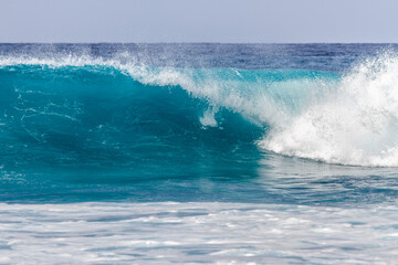 Waves coming ashore on a sunny day. Blue wave wall with white foam coming ashore where surfers surf. Atlantic Ocean. Tenerife, Canary Islands, Spain.