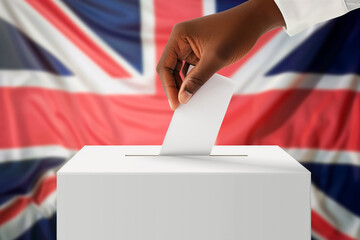 Close-up of a man's hand who throws a ballot paper with his vote in an election with the flag of the UK in the background