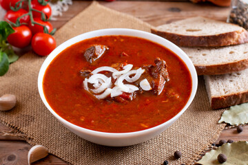 Pork goulash meat on plate, garlic, onion, tablecloth in the background - typical Czech food