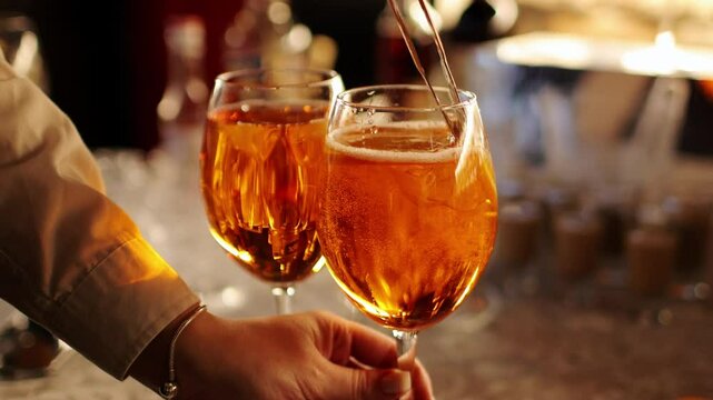 Bartender makes two glasses of cocktail Aperol spritz on bar counter, adds fresh orange slices. Typical alcoholic Italian beverage, aperitif made with Prosecco sparkling white wine and ice cubes