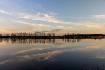Obraz premium a row of trees without foliage and a lake shore at sunset in spring