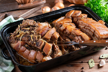 Piece of baked pork belly served with onions and mushrooms on a baking tray served on a wooden table, typical Czech food
