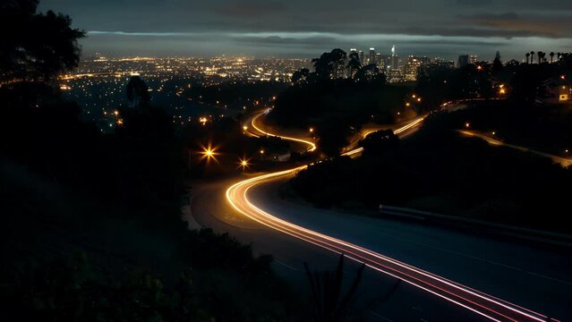 The city glows in the distance as cars travel along a twisty hillside drive creating light trails.